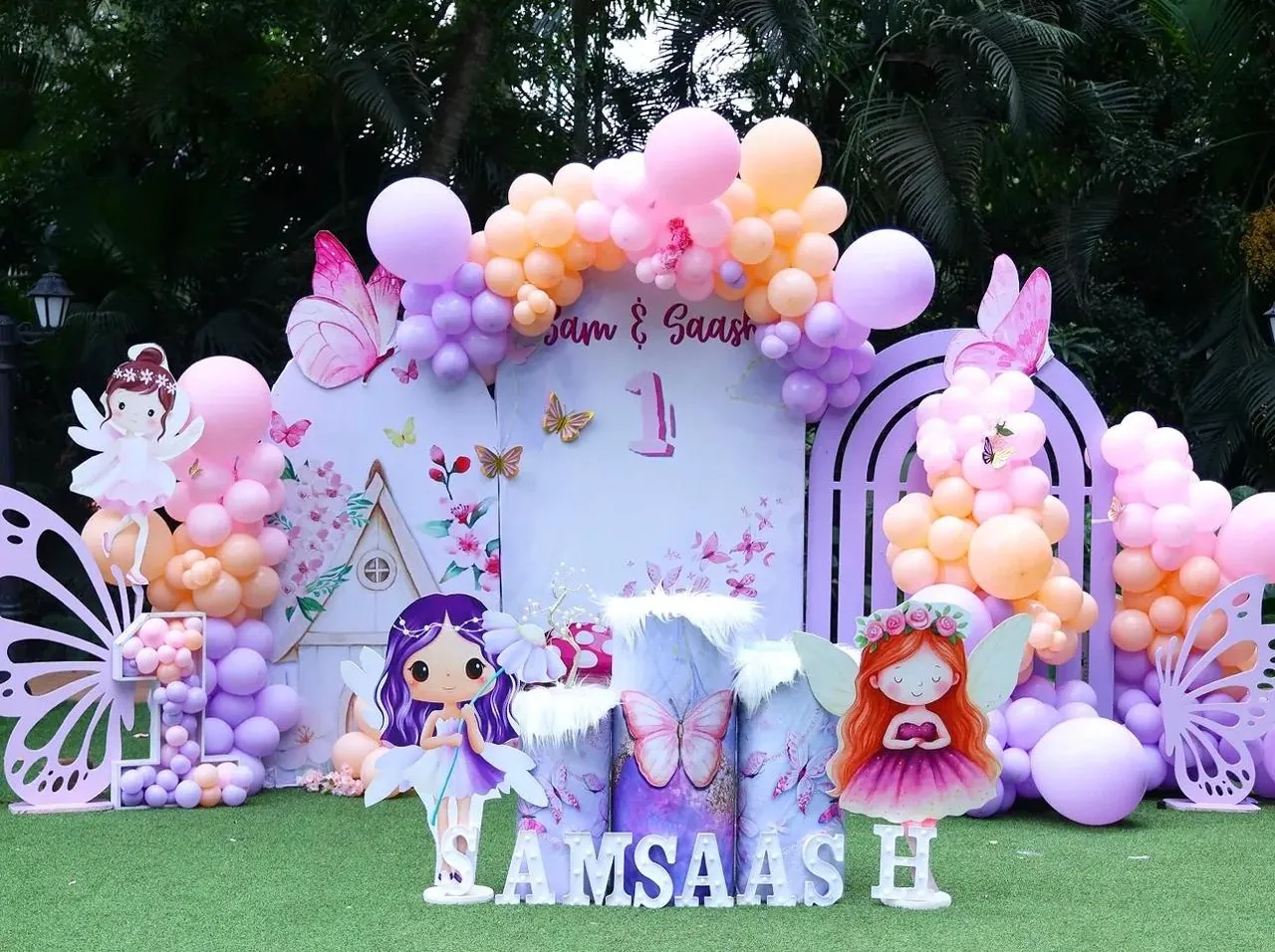 Outdoor first birthday stage with a floral arch and fairy props