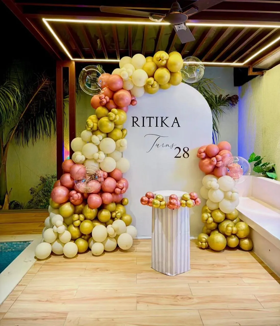 Gold and blush balloon arch beside a poolside terrace